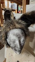 Brown and black furry hat with large rounded ears, resembling a werewolf or similar animal hat displayed on a mannequin head.