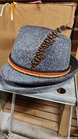 Gray felt Bavarian hat with black, red, yellow braided band and long feather attached.