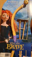Photo of the Merida Brave licensed bow and arrows set in vendor packaging, showing toy bow and two suction-cup arrows with Disney Pixar Brave branding and character artwork.