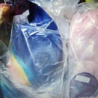 Photo showing multiple specialty cosplay wigs in festival colors including rainbow and pastel pink, sealed in vendor packaging plastic bags.