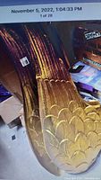 Photo showing close-up of several large gold plastic wings stacked together, detailing the feather pattern and gold paint finish.