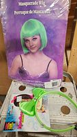 Short bob bright green masquerade wig packaging showing a woman wearing the wig in front. Also shown is a green bow headband outside the packaging on a table.