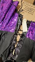 Close-up photo of purple and black sequined stand up collar with lace-up detail and attached tag.
