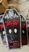 Close-up photo of medium Sexy Devil Bites vampire fangs in original black coffin-shaped packaging with red text and a vampire face graphic