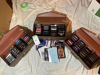Three open brown hinged carrying cases each filled with two rows of Atari 2600 cartridges laid out on a white sheet.