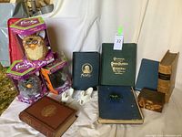 Full lot overview showing antique books, boxed Furbies, white ceramic swan figurines, and a small green frog figurine.