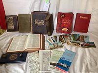 Full lot view showing books, postcards, maps, pouch and pins arranged on white cloth background