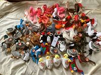 Overview of entire lot showing various Beanie Babies placed across a bed including flamingos, turkeys, bears, chicks, and other birds all with Ty tags.