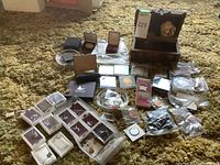 Photo showing a variety of collectible coins in protective cases and some loose coins along with small jewelry items and a wooden box containing the puppy statue figurine