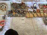 Overview of five plastic trays containing assorted vintage costume jewelry pieces spread on white cloth