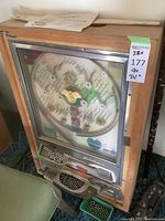 Front view of pachinko machine in wooden cabinet showing glass playfield and metal controls
