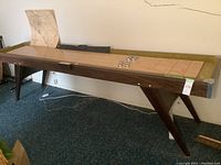 Side view of entire shuffleboard table showing dark-stained wood legs and butcher-block playing surface.