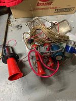 Photo showing multiple red plastic and metal air horns tangled with wiring along with two rectangular vehicle lights.