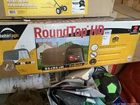 Box showing Round Top HD Auto Shed branding, dimensions 12x20 ft, brown curved cover car shelter