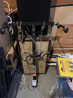 Full front view of a black metal Hitch Factory bicycle hitch rack with two hooks and securing straps displayed upright against a speaker or box.