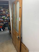 Side angle view of entire wooden door showing its structure, two clear vertical glass panes, and vintage metal handle/latch hardware.