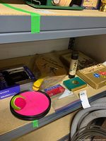 View of Franklin Paddleball paddle with two black balls in clear plastic bag alongside vintage board games, cards, Pick up Sticks sticks, and Sony Walkman in box on shelf