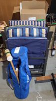 Photo showing two folding lawn chairs with striped cushions and one blue cushioned lounge chair stacked together, croquet carrying bag in front