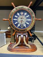 Front view of ships wheel clock with nautical rope knot hour markers and brass accents on wood base with rope detail.