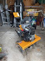 Side view of an upright yellow and black gas-powered tiller with rotating tines and pneumatic wheels