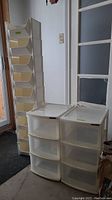 Front view of one tall resin storage cubby unit with nine cubbies and two smaller drawer units with three drawers each, placed together on floor.