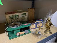 Photo shows green Coleman Summelite Plus picnic stove, metal burner with wind guard, folded handle, stove box with vintage graphics, small brass oil lamp with glass chimney, some rust. Accessories and boxes around.
