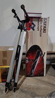Silver tripod with black mounting bracket beside Safari 525x reflector telescope box and hardcover book on skywatching
