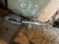 Full view of trailer dolly showing the single wheel, steel frame, mounting bracket and locking pin, placed on floor with light dust and dirt.