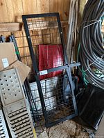 Front view of the metal rack showing wire mesh surface and surrounding frame leaning against shed wall.