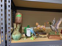 Shelf view of two Blue Mountain Pottery vases (beige tall, smaller green-brown), green lidded dish, brass eagle, carousel cat, ceramic duck, Beswick bird, parakeet with chips