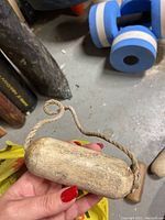 Hand holding a small, aged wooden fishing float with a rope attached against a cellar floor background.