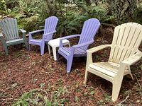 Four Adirondack chairs in the forest setting: two pale purple, one off-white, with a matching small off-white side table between the purple chairs. All furniture has dirt and outdoor wear.