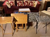 View of all trays and tables arranged in front of sofa, showing all seven pieces including four wooden trays, two leopard print tables, and one wooden bed tray