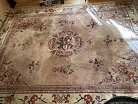 Full view of the large area rug showing the faded rose and cream floral design with a beige background and decorative border.