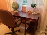Photo showing wooden desk with globe, clock, desk lamp, and brown office chair from side angle