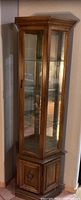 Full view of tall corner curio cabinet showing wood finish, glass panels, and lower storage cabinet with door.