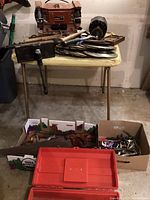 Full view of the lot showing the Edison bench grinder on a folding table with an assortment of hand tools, saw blades, and a vintage table clamp on the floor and table surface.