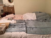 Overall view of six sets of king-size sheets and linens, showing pink, blue, and white linens, some folded and some in packaging.