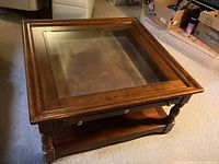 Square wooden coffee table viewed diagonally showing inset glass top and wear on edges.