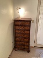 Front view of tall 7-drawer wooden lingerie chest with lamp on top, chest has slight wear on front drawers.