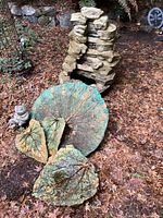 Ceramic rock-style fountain with stacked stone appearance and three large ceramic leaf decorative plates on leaf-covered ground.