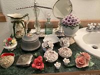 Overview of the vanity items including ceramic pitcher, porcelain flowers, metal boxes, mirror, and glass bottle