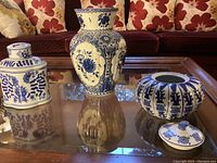 Photo of three blue and white vases with floral and ornamental designs on a glass table.