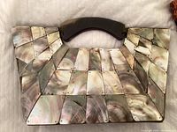 Close-up of shell clutch handbag showing marbled rectangular shell panels and dark handle