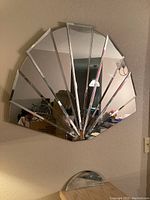 Vintage fan shaped mirror affixed on a wall, showing multiple vertical mirrored panels fan-like arranged