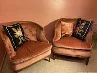 Pair of vintage velvet barrel armchairs positioned side by side, each with two decorative throw pillows