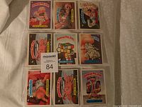 Photo of 9 Garbage Pail Kids character cards arranged in plastic sleeves, showing colorful illustrations and staples