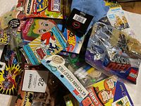 Overhead view of many small toys including packaged Hot Wheels and Matchbox cars, LEGO Ninjago minifigure pack, Beyblade spinner, markers, plastic army men figures, and other assorted toys.