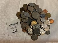 Pile of various foreign coins with diverse sizes and colors on a light-colored surface.