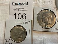 Photo showing two collectible U.S. coins housed in cardboard holders: a 1967 Kennedy Half Dollar and a 1974 Eisenhower Dollar.